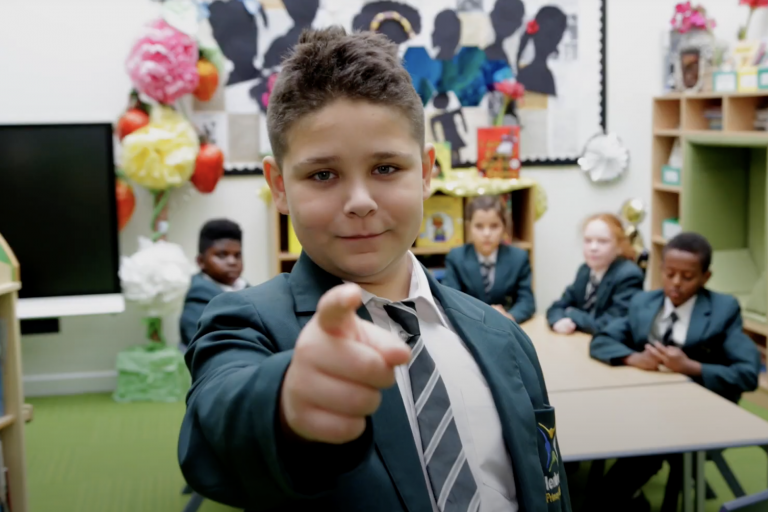 Boy in classroom pointing finger at camera