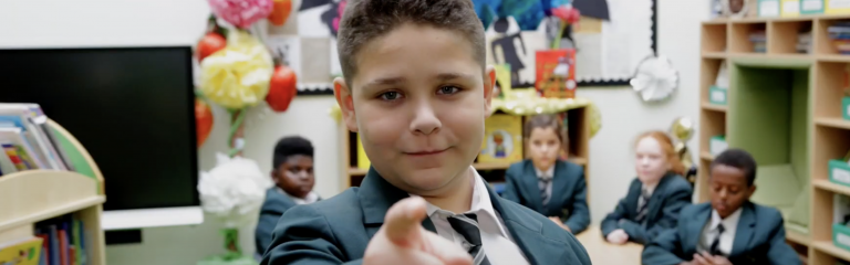 Boy in classroom pointing finger at camera